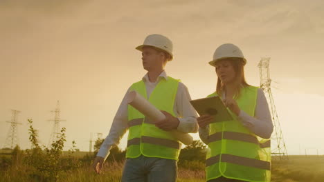 ingenieros de coworking con tabletas en la planta solar. hombres y mujeres adultos con cascos usando tabletas mientras están al aire libre en la plataforma de transformadores. transporte de energía limpia. entrega de energía eólica