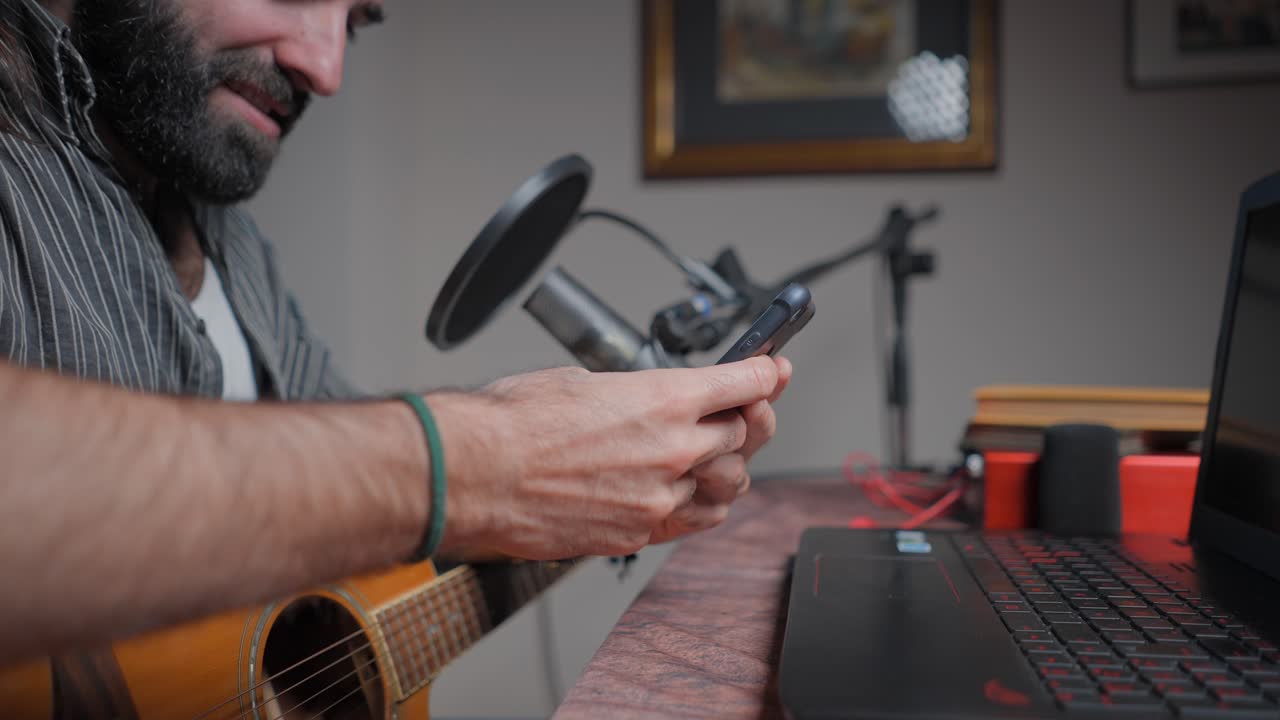 Man Playing Guitar and Using Phone in Home Recording Studio
