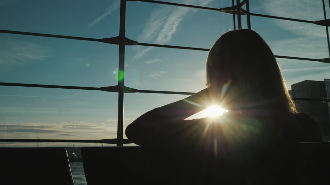 여자는 여행을 기대하며 공항 터미널의 큰 창으로 앞으로 쓸어갈 것입니다.