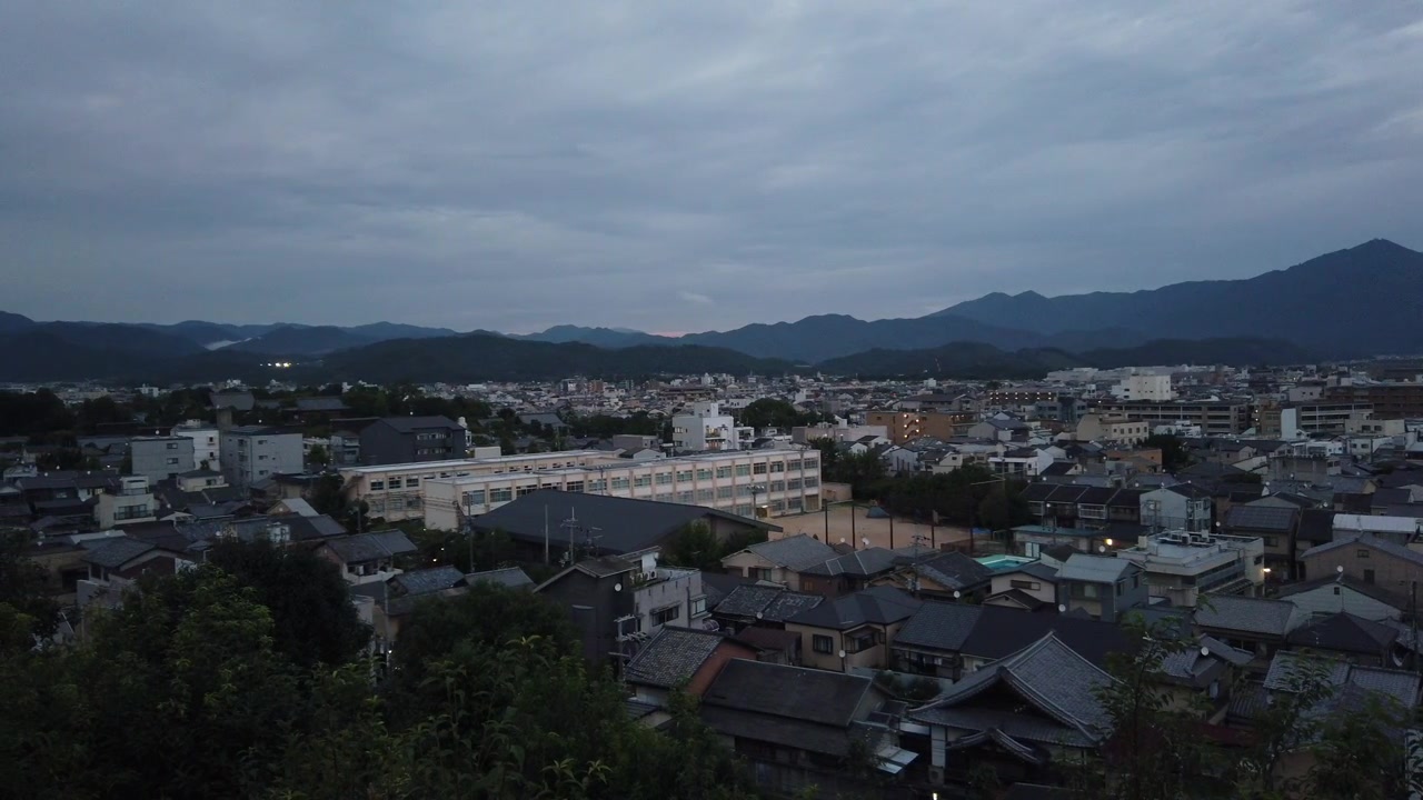 Ampia veduta aerea di Kyoto, Giappone, atmosfera di quartiere giapponese al crepuscolo, sera con sfondo montuoso, campo sportivo del campus scolastico e alberi