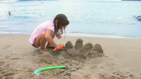 ragazza che gioca sulla spiaggia costruendo castelli di sabbia