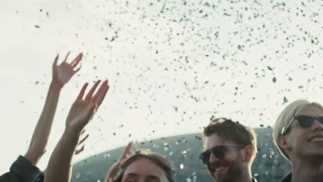 young caucasian friends dancing among confetti on music festival with hands up