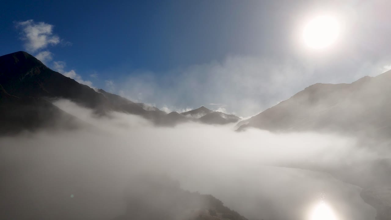 Drone captures serene sunrise over mist-covered mountains in Queenstown, New Zealand. Crisp winter air and clear skies enhance the scene