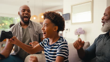 multi-generation male family sitting on sofa at home playing video game together