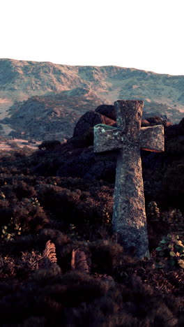 cruz de piedra en un campo con montañas en el fondo