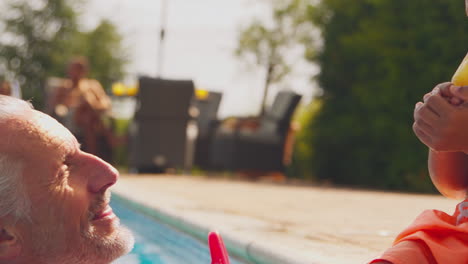 Abuelo-Y-Nieto-Comiendo-Polos-De-Hielo-En-El-Borde-De-La-Piscina-Durante-Las-Vacaciones-Familiares-De-Verano