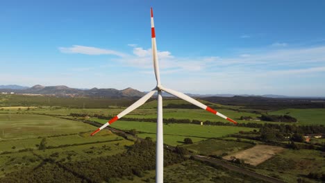 Single-Wind-turbine-with-painted-red-stripes-rotating-in-rural-landscape,-aerial