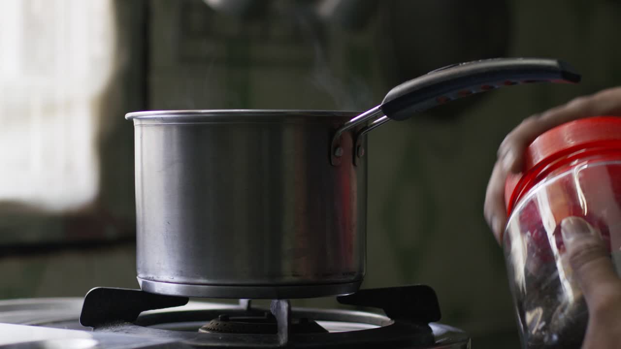 A slow-motion of hands opening a jar near a steaming metal pot on the stovetop against a blurred background