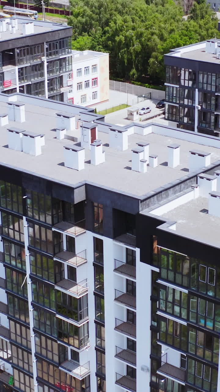 Modern apartment buildings in the city. New residential complex with high-raised buildings of modern design. Roofs of multi-storey buildings on urban background. Aerial view. Vertical video