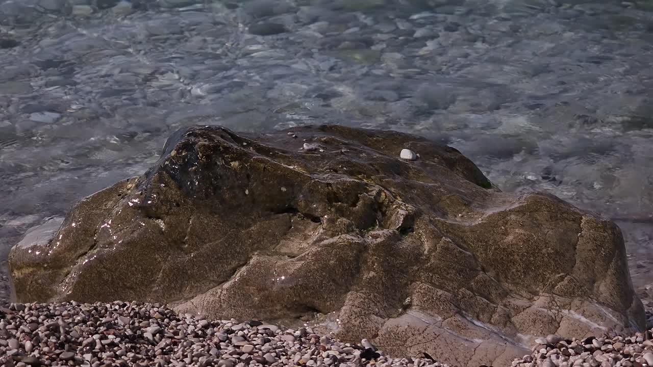 Pietra sulla spiaggia bagnata da acqua marina cristallina all'alba, con sfondo marino e spazio per testo per vacanze.