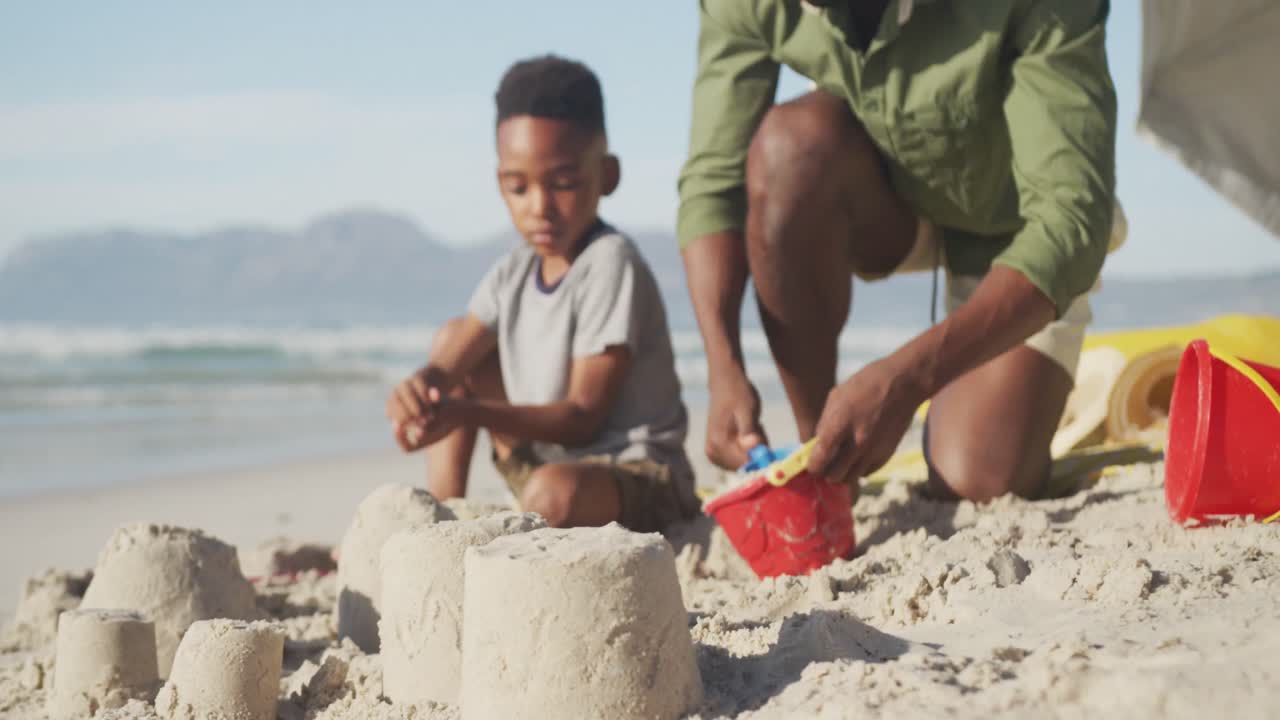 아프리카계 미국인 아버지 와 아들 이 해변 에 있는 모래 에서 놀고 있다