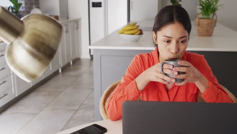 mujer biracial usando computadora portátil y trabajando en la cocina