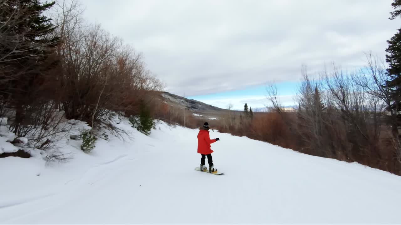 una snowboarder femenina bajando por un hermoso camino nevado en una estación de esquí en colorado con colores naranja y rojo del desierto en el fondo