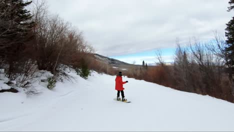 Eine-Snowboarderin,-Die-Einen-Wunderschönen-Verschneiten-Pfad-In-Einem-Skigebiet-In-Colorado-Hinuntergeht,-Mit-Orangen-Und-Roten-Wüstenfarben-Im-Hintergrund