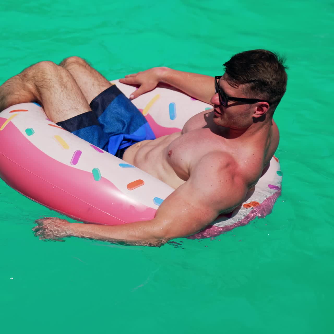 Man wearing sunglasses resting in the sun. Man sits in the inflatable circle in the pools rowing with hands