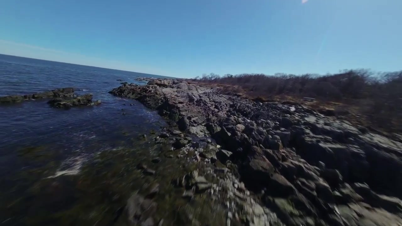 Un drone FPV sfreccia in avanti, volando appena sopra l'acqua e serpeggiando tra le aspre rocce costiere lungo la splendida costa del New Hampshire.