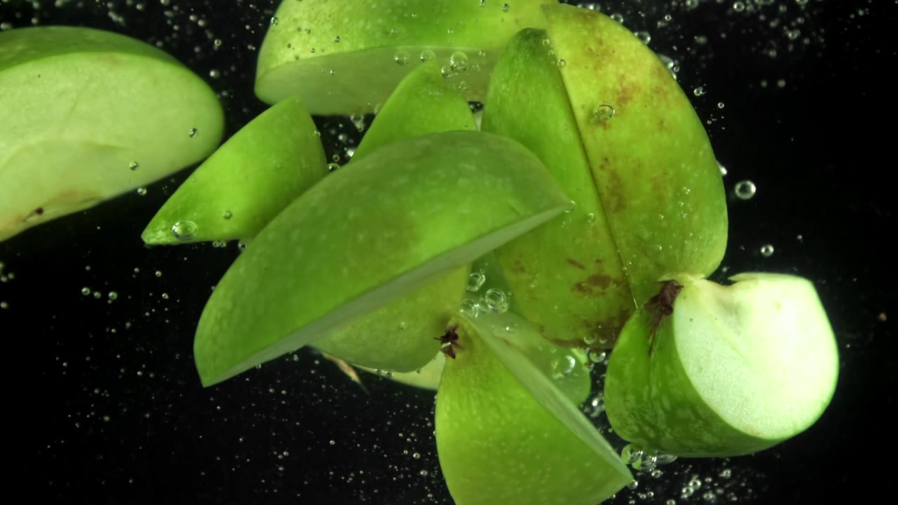Fette di mela verde fresca che galleggiano nell'acqua con bollicine