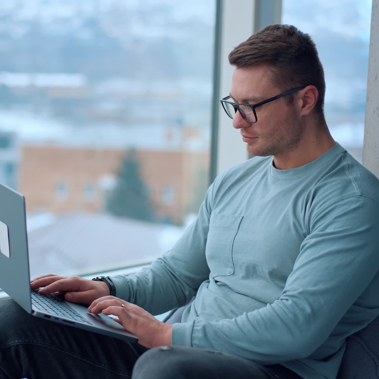Busy focused man in glasses looks attentively at the screen of his laptop. Freelancer distracts from work for a moment glancing into window