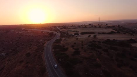 Drohnenaufnahmen-Aus-Der-Luft-Einer-Malerischen-Ländlichen-Straße-Mit-Einem-Weißen-Pick-up-Auto,-Das-Von-Oben-Zum-Sonnenuntergang-Führt