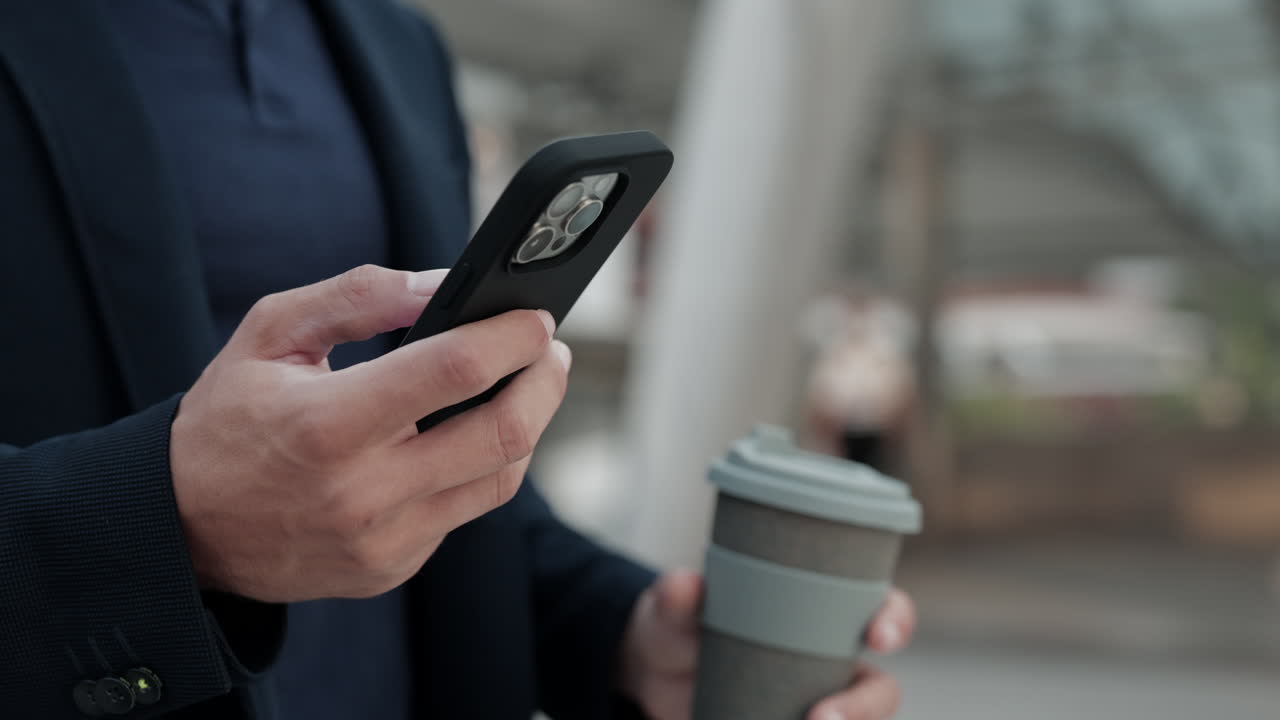 Close-up of Man's Hands Using Smartphone and Holding Coffee Cup
