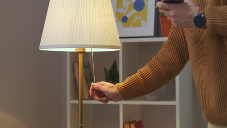 man is turning off floor lamp in living room or bedroom at evening interior of modern apartment closeup view