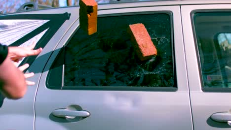 dos ladrillos de arcilla roja siendo arrojados a una ventana lateral de los coches rompiendo el vidrio en cámara lenta