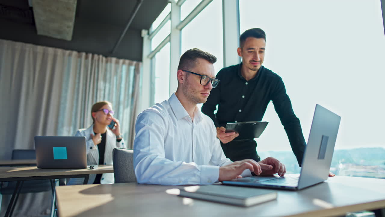 Male colleagues in the office working using computer. Positive woman at desk behind speaks on the phone. Low angle view.