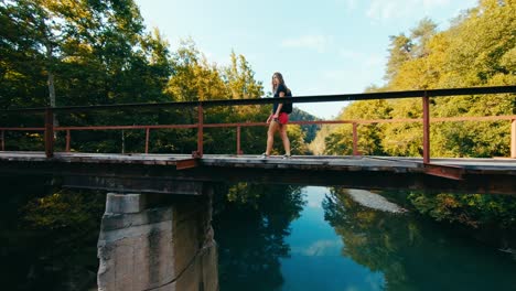 Reveladora-Toma-De-Drones-De-Una-Mujer-Viajera-Mirando-La-Vista-En-El-Viejo-Puente-Ferroviario-De-Madera-En-El-Otoño