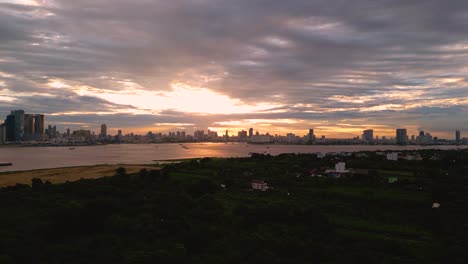 drone shot of phnom penh urban city skyline buildings, mekong riverfront green forest with sunset sky