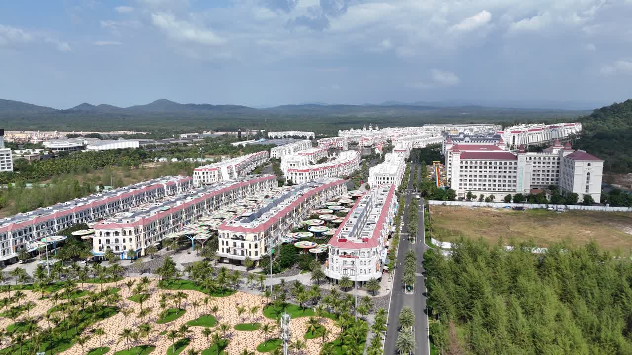 An aerial video taken in the afternoon a newly built town's architectural style by colorful buildings. Wide roads and emerging green spaces are evident, beautifully framed by a distant range of hills