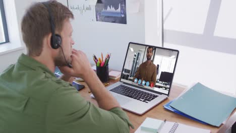 hombre caucásico con auriculares de teléfono haciendo una videollamada con un colega masculino en una computadora portátil en la oficina
