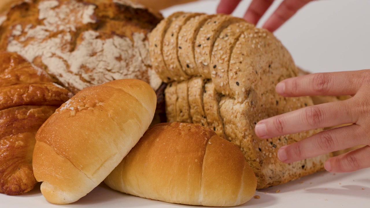 Close-up shot of hands organizing various fresh bakery items against a clean white background.