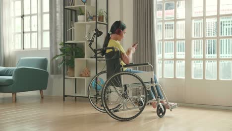 asian kid girl sitting in a wheelchair listening to music and using mobile phone