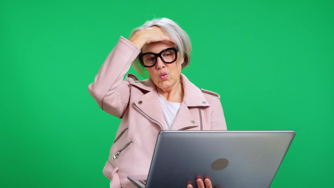 Stressed senior businesswoman working on laptop on green screen