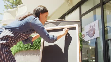 animation of happy biracial waitress writing on blackboard at coffee shop