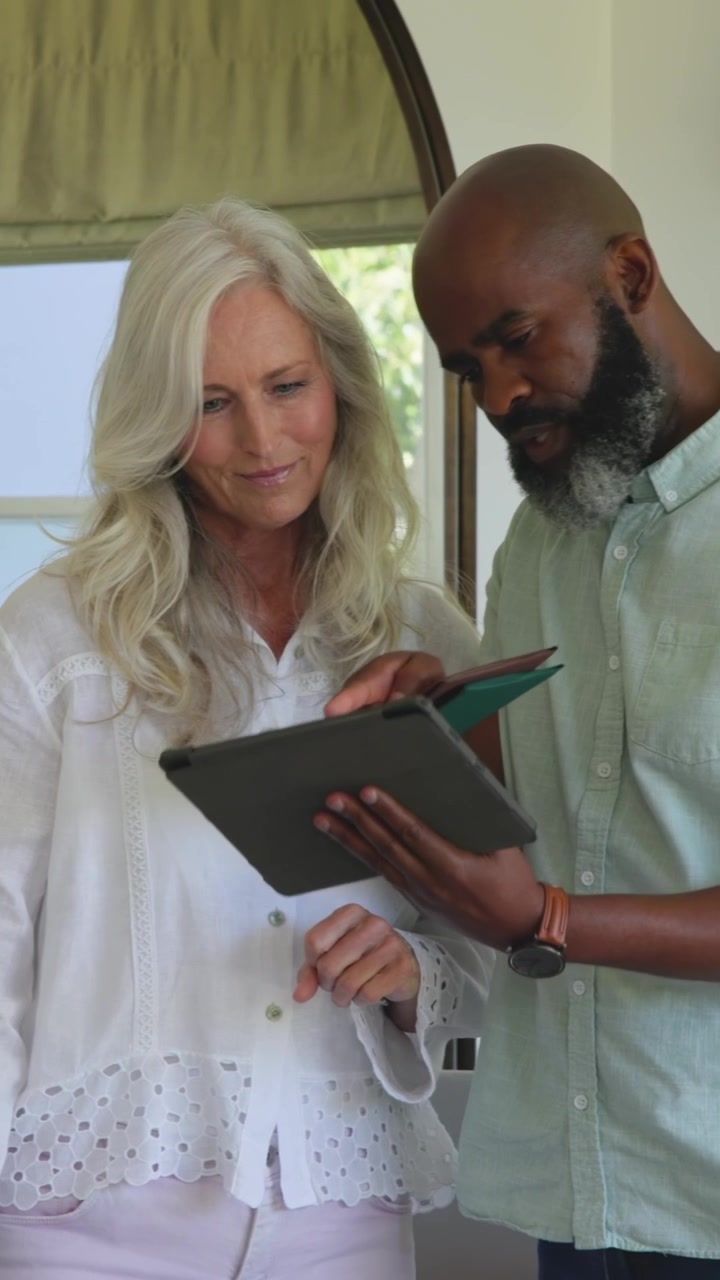 Woman pointing at laptop, man nudging tablet, fetching bag, comparing tablet and card for business