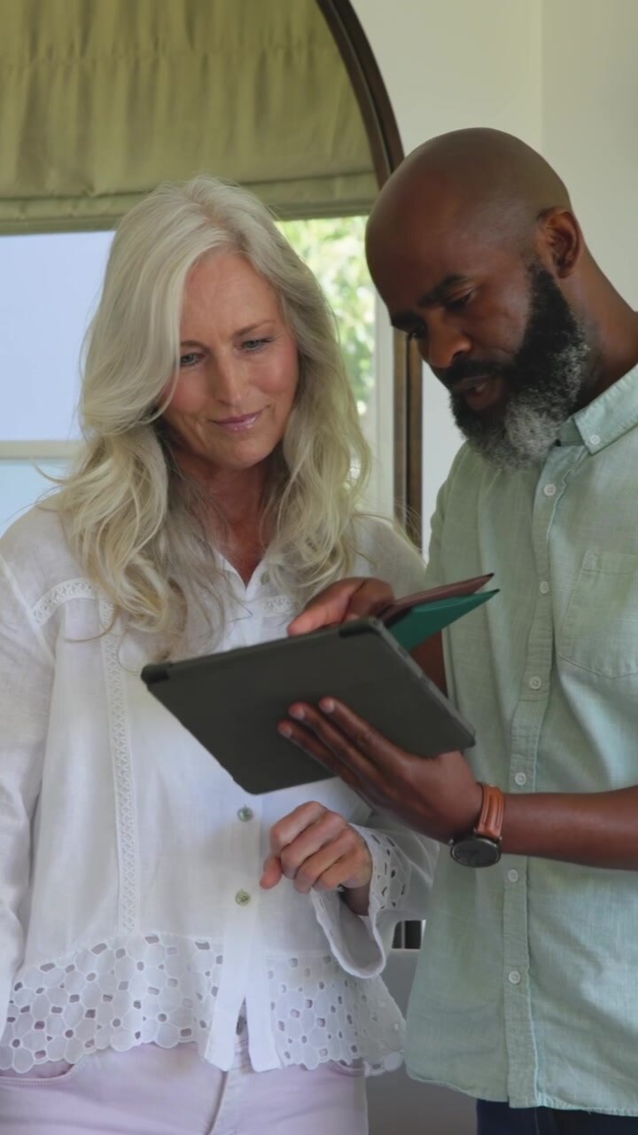 Woman pointing at laptop, man nudging tablet, fetching bag, comparing tablet and card for business