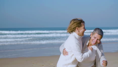 happy senior women having fun and hugging on ocean shore