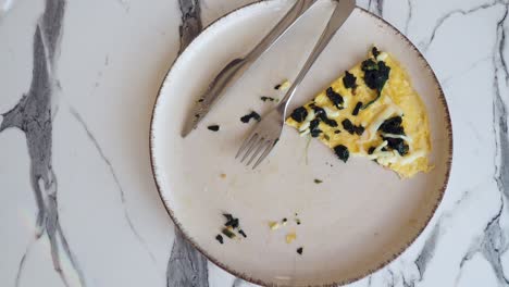 un plato con una tortilla de espinaca a mitad de comer, con un tenedor y un cuchillo en el lado.