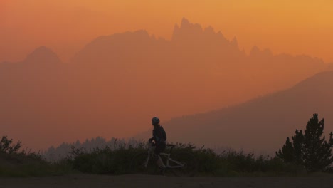 un ciclista de montaña se detiene en una ladera al atardecer y toma una foto