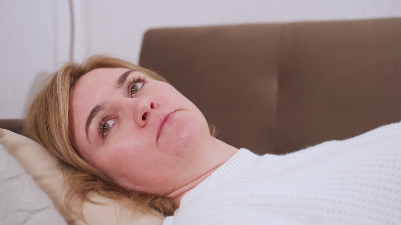 Close up of woman lying face up on couch speaking directly toward camera, expressive conversation scene captured from side angle, natural lighting highlighting facial features during dialogue