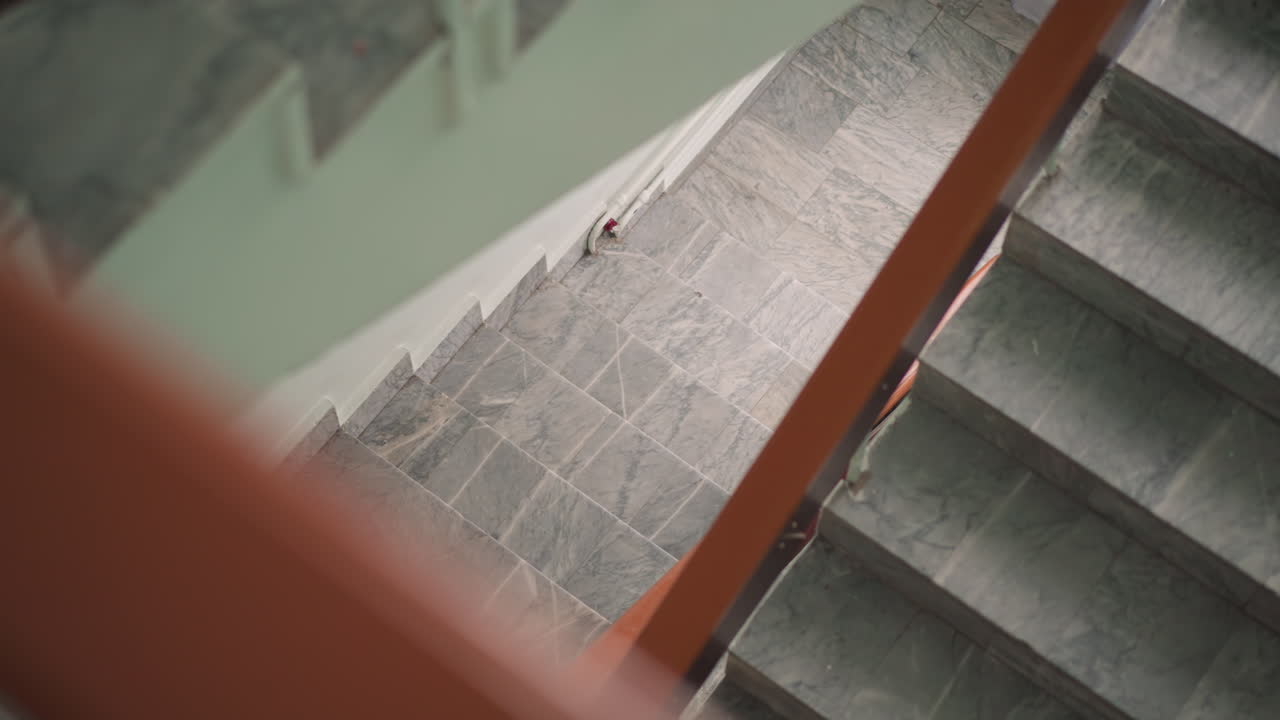 Aerial view of woman in white top and black leggings carrying black school bag while climbing stairs, soft indoor light creating urban atmosphere with focus on upward motion and daily lifestyle