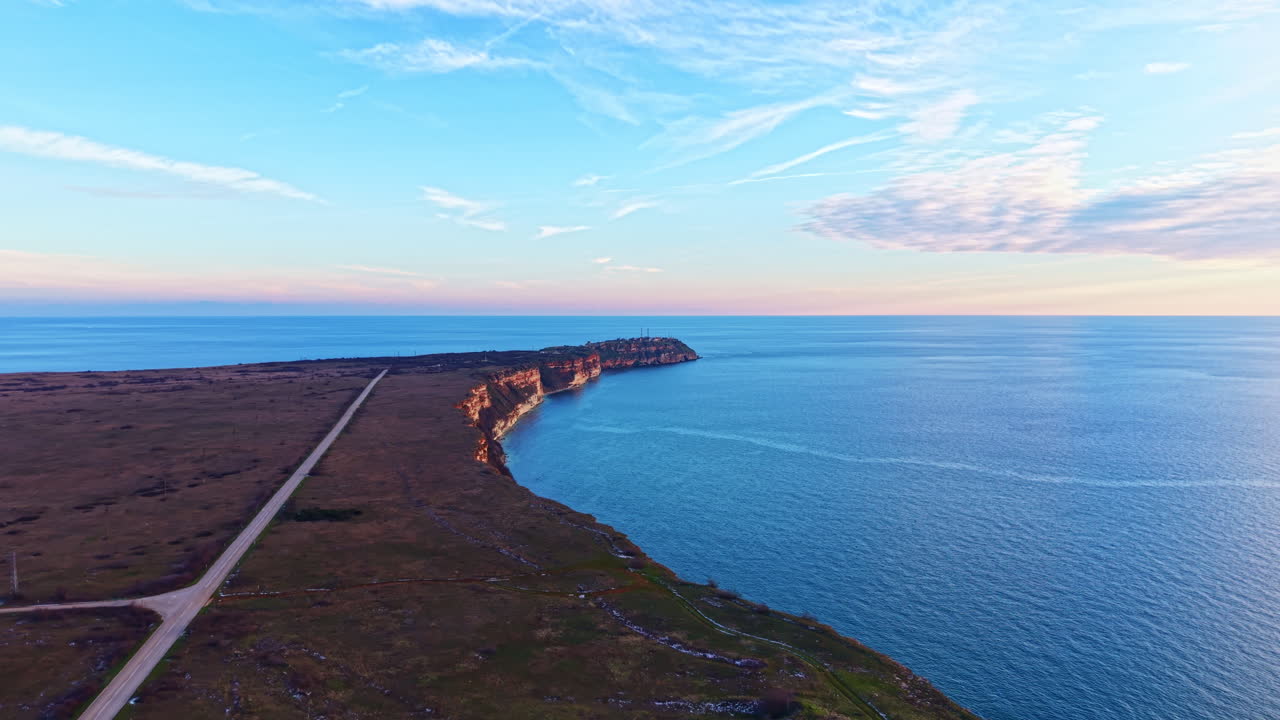 Naturskjønn utsikt over kystland som møter havet i skumringen, med klar himmel og fjerne klipper i sikte