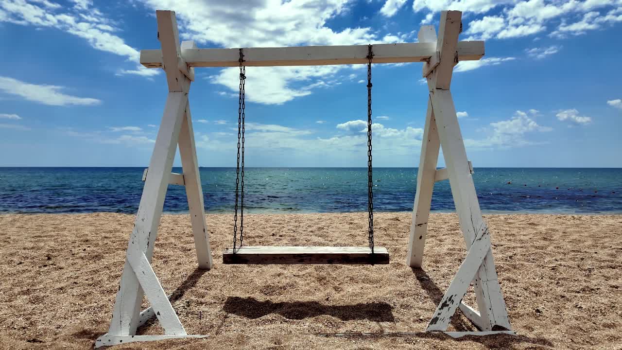 un columpio de madera en una playa de arena en crimea, frente al mar azul claro