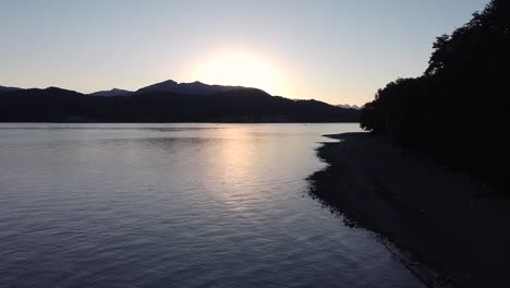 Toma-Cinematográfica-De-Establecimiento-Moviéndose-Hacia-Atrás-Desde-El-Lago-Nahuel-Huapi-Al-Atardecer-En-Villa-La-Angostura,-Patagonia-Argentina