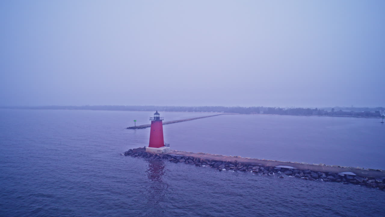 Aerial shot of a lighthouse on a misty day over Lake Michigan's breakwater.