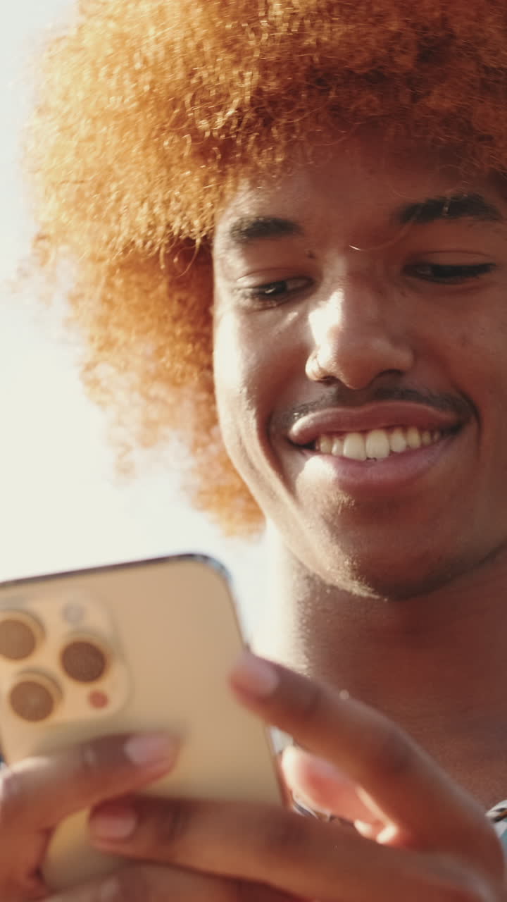 Giovane uomo con capelli ricci arancioni che sorride mentre usa lo smartphone