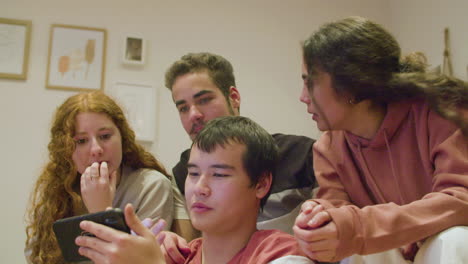 friends sitting in living room, watching match on mobile phone