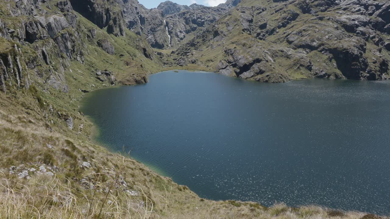 View of Harris lake, mountains and a waterfall on a sunny summer day at Routeburn Track, New Zealand.