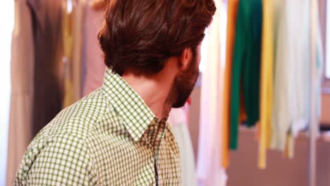 bored man sitting while woman selecting clothes from clothes rail